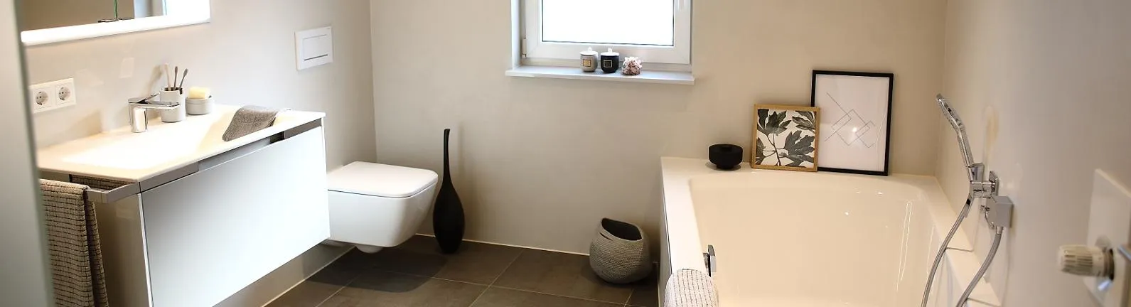 Helles modernes Bad mit Waschtisch, Wand-WC und Badewanne, dekoriert mit Accessoires und Bildern.