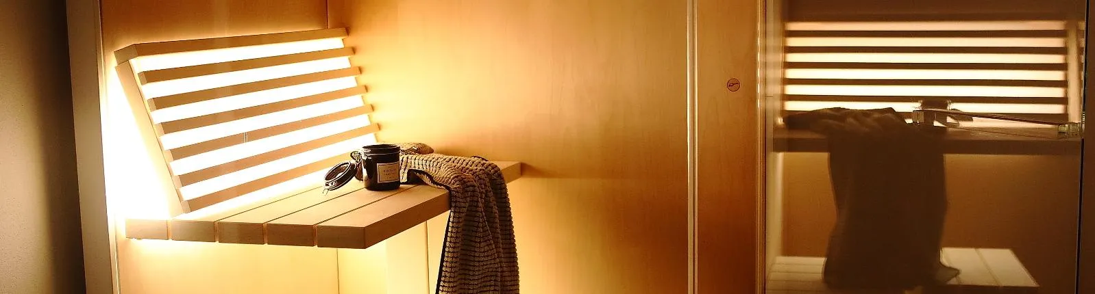 Sauna-Innenraum mit beleuchteter Holzbank, dekoriert mit Handtuch und Duftkerze, stimmungsvolles warmes Licht.