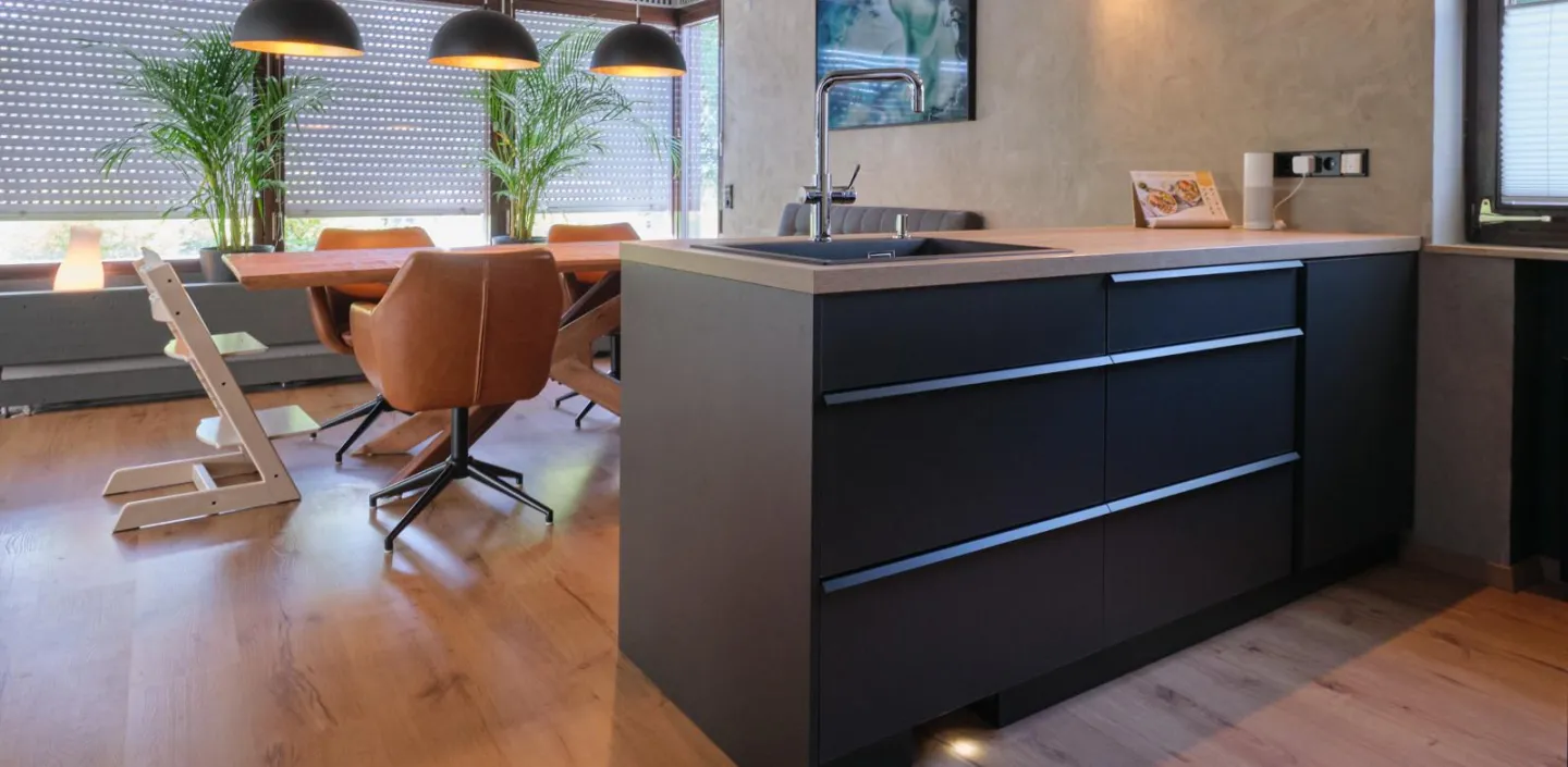 Moderne Wohnküche mit schwarzer Kochinsel, Holzboden und gemütlicher Essgruppe mit Lederstühlen.