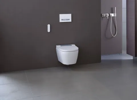 Dieses Badezimmer verfügt über ein wandhängendes Geberit AquaClean Dusch-WC, kombiniert mit einem edlen Waschtisch aus dunklem Holz und einer verchromten Wasserarmatur.