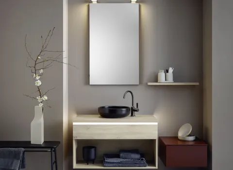Dieses Badezimmer kombiniert moderne Elemente wie ein schlichtes Waschbecken aus schwarzer Keramik und einen beleuchteten Spiegel mit natürlichen Akzenten.