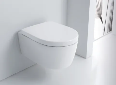 Eine minimalistische, wandmontierte Toilette in Weiß mit abgerundetem Deckel, die nahtlos an eine weiße Wand angepasst ist.