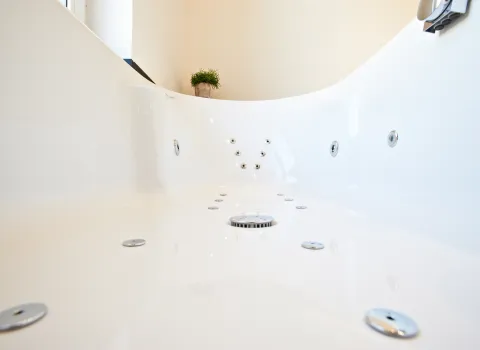 Nahaufnahme des Innenraums einer modernen Whirlpool-Badewanne mit mehreren eingelassenen Düsen und einem runden Abfluss in der Mitte. 