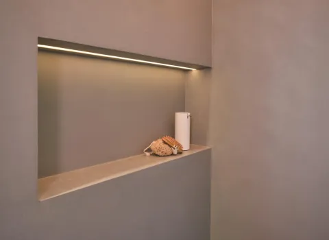In die Badezimmerwand integriertes Ablagefach mit indirekter LED-Beleuchtung, dekoriert mit Seifenspender, Bürste und Schwamm.