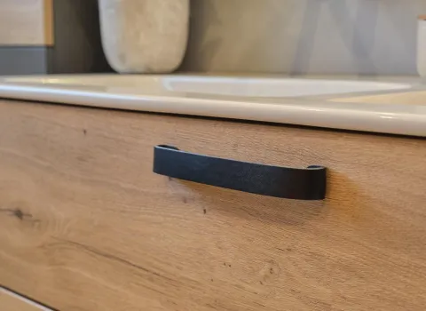 Detailaufnahme des Waschtischunterschranks in Holzoptik mit schwarzem Ledergriff.