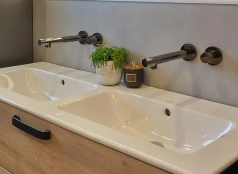 Moderner Doppelwaschtisch in Holzoptik mit zwei Aufsatzarmaturen, dekoriert mit Pflanze und Kerze.