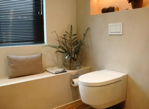 Modernes WC im Wohnbad mit dekorativer Sitzbank, Pflanze in Glasvase, Holzfußboden und beleuchtetem Wandfach.