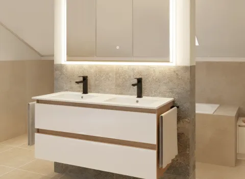 Ein moderner Doppelwaschtisch mit weißen Fronten und dunklen Armaturen steht vor einer Natursteinwand. Darüber befindet sich ein beleuchteter Spiegelschrank mit integrierter LED-Leiste. Der Waschtisch bietet zwei Handtuchhalter an den Seiten. Die Gestaltung ist funktional und elegant.