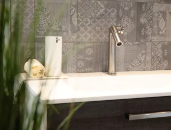 Moderner Waschtisch in Holzoptik mit Edelstahl-Armatur, Seifenspender und Handtuch vor grauer Fliesenwand.