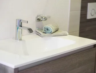 Moderner Waschtisch mit verchromter Armatur, Handtüchern und Glas-Seifenhalter in Holzoptik-Unterschrank.