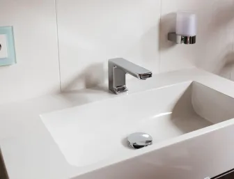 Weißer Waschtisch mit moderner verchromter Armatur und Wand-Seifenhalter in minimalistischer Badgestaltung.