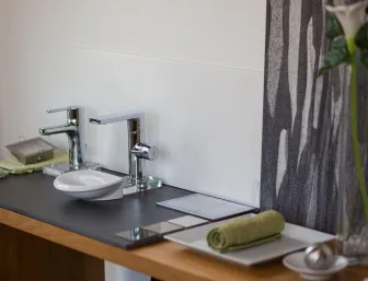 Ausgestellter Waschplatz mit zwei modernen Armaturen, Seifenschale, Handtuch und Musterfliesen in der Badausstellung.