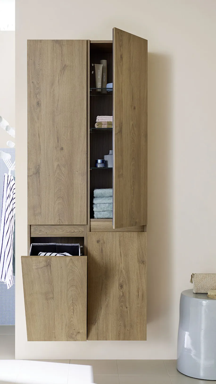 Ein hoher, hölzerner Badezimmerschrank mit mehreren Fächern, von denen einige geöffnet sind und Handtücher sowie Pflegeprodukte zeigen.