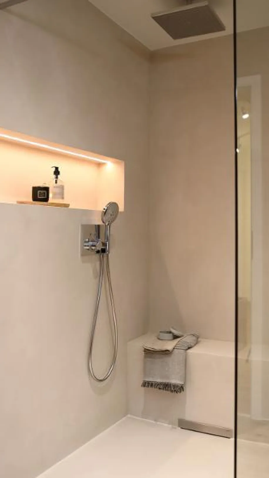 Moderne Dusche mit Regenbrause, integrierter Ablage mit Beleuchtung, Handbrause und Sitzbank.