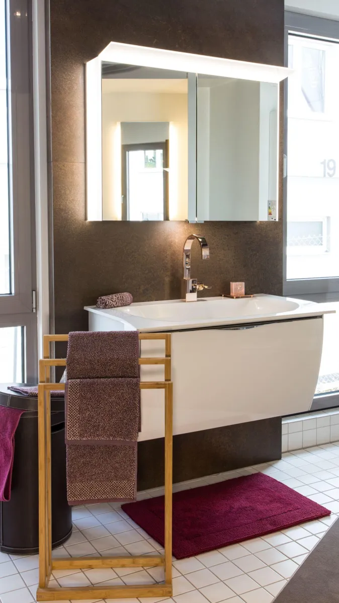 Moderner Waschplatz mit weißem Waschtisch, LED-Spiegelschrank, roségoldener Armatur und dekorativen Handtüchern in Beerentönen.