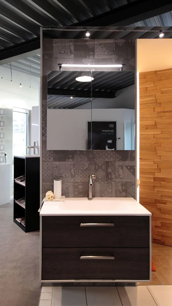 Ausgestellter Waschplatz mit dunklem Unterschrank, rechteckigem Becken, Edelstahlarmatur, LED-Spiegel und Rückwand aus gemusterten Fliesen.