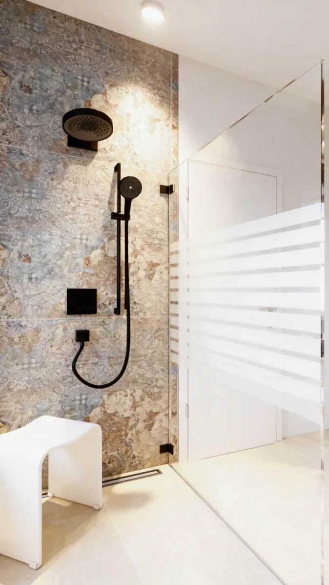 Eine moderne Walk-in-Dusche mit Regenbrause und Handbrause in mattem Schwarz. Die Wand ist mit strukturierten Natursteinfliesen gestaltet. Eine Glaswand mit Milchglasstreifen trennt den Duschbereich ab. Ein weißer Hocker sorgt für Komfort.