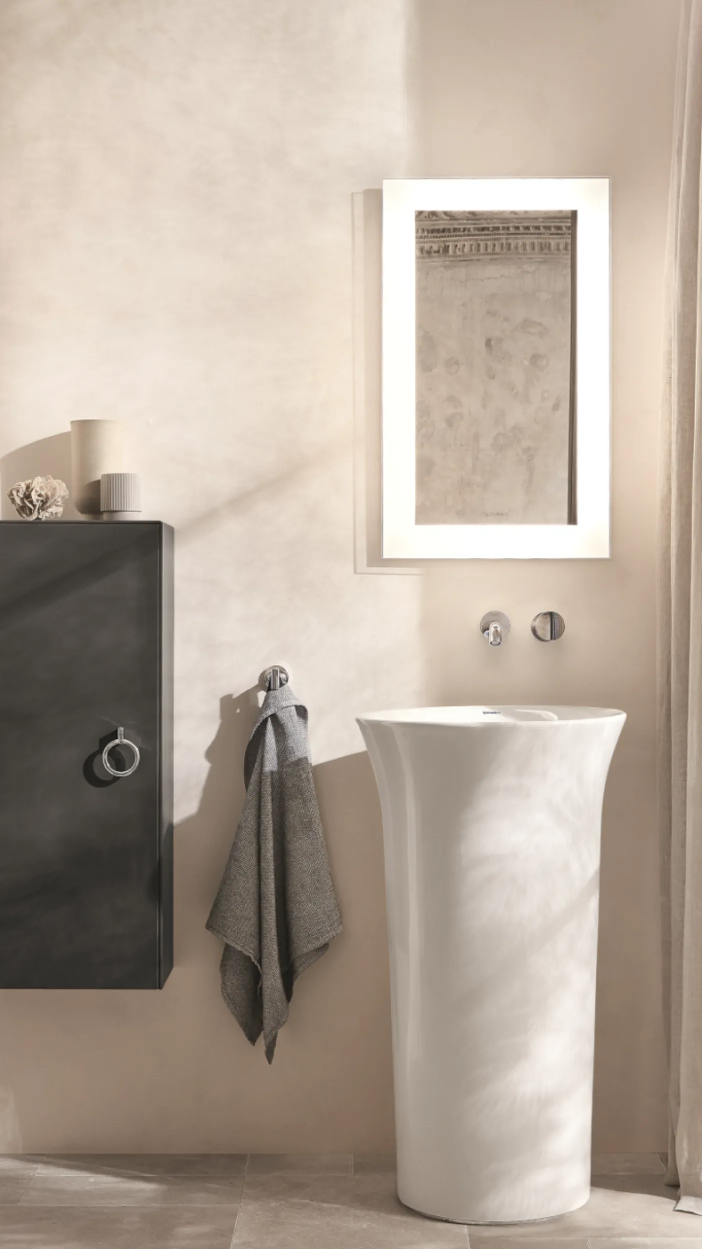 Ein minimalistisches Badezimmer mit einem eleganten, weißen Standwaschbecken und einem beleuchteten Spiegel darüber.