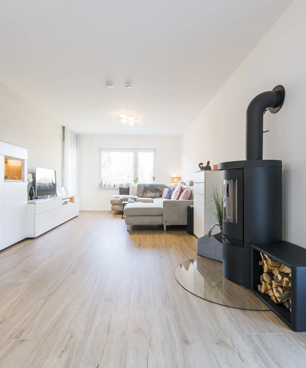 Heller Wohnraum mit Holzboden, schwarzen Kamin, weißen Möbeln und Fenster.