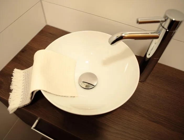Modernes Gäste-WC mit rundem Aufsatzwaschbecken auf Holzkonsole und verchromter Armatur.