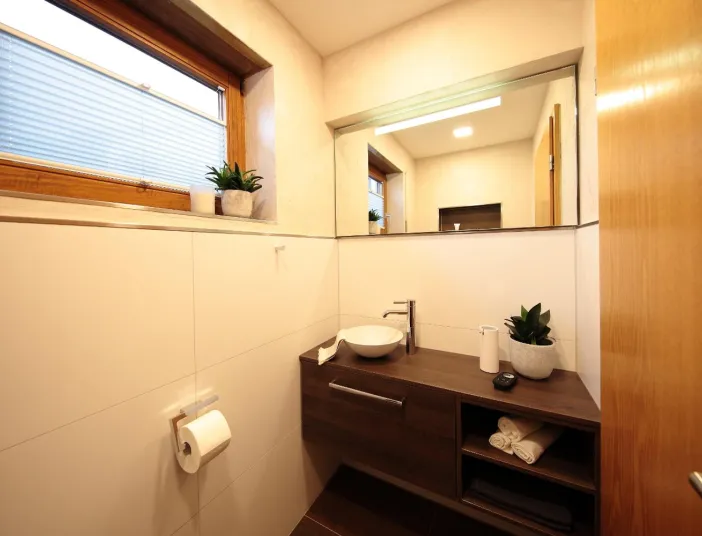 Gäste-WC mit Holzwaschtisch, rundem Aufsatzwaschbecken, großem Spiegel und Fenster mit Pflanzendeko