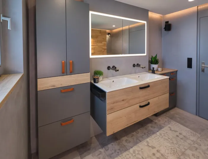 Modernes Kompaktbad mit Doppelwaschtisch in Holzoptik, grauen Badmöbeln mit Lederschlaufen, großem LED-Spiegel und dekorativen Bodenfliesen.