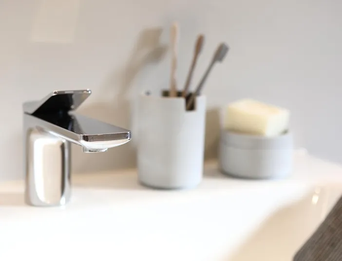 Detailaufnahme eines modernen Waschbeckens im Komplettbad mit verchromter Armatur, Seifenschale und Zahnbürstenhalter.