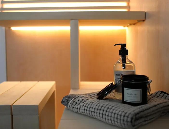 Detailaufnahme in der Sauna mit Handtuch, Duftkerze und Seifenspender auf einer Holzbank mit stimmungsvoller Beleuchtung.