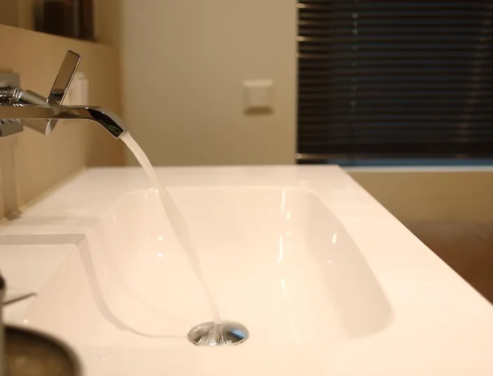 Detailaufnahme eines modernen Waschtischs mit Wandarmatur, aus der Wasser in das Becken fließt.