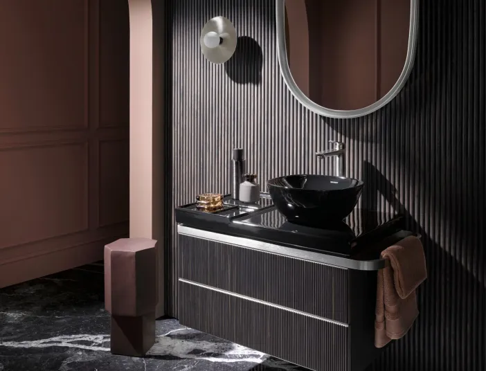 Hochwertiges Badezimmer in sehr dunkler Farbgebung inklusive eines dunkelbraunen Waschtischunterschranks mit schwarzem Aufsatzwaschbecken und schwarzweißen Natursteinboden.