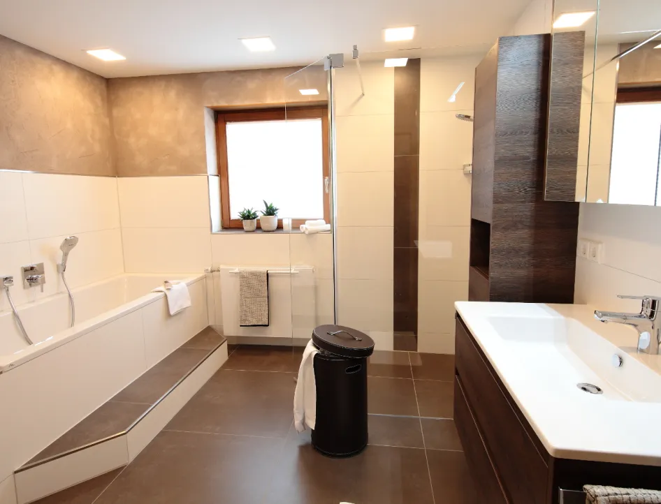 Großzügiges Bad mit Badewanne, ebenerdiger Dusche, Holz-Waschtisch und modernen Fliesen in Naturtönen.
