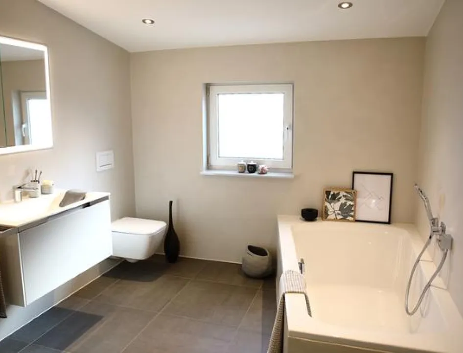 Komplettbad in modernem Design mit Waschtisch und Spiegel, Wand-WC, Fenster und Badewanne mit Handbrause.