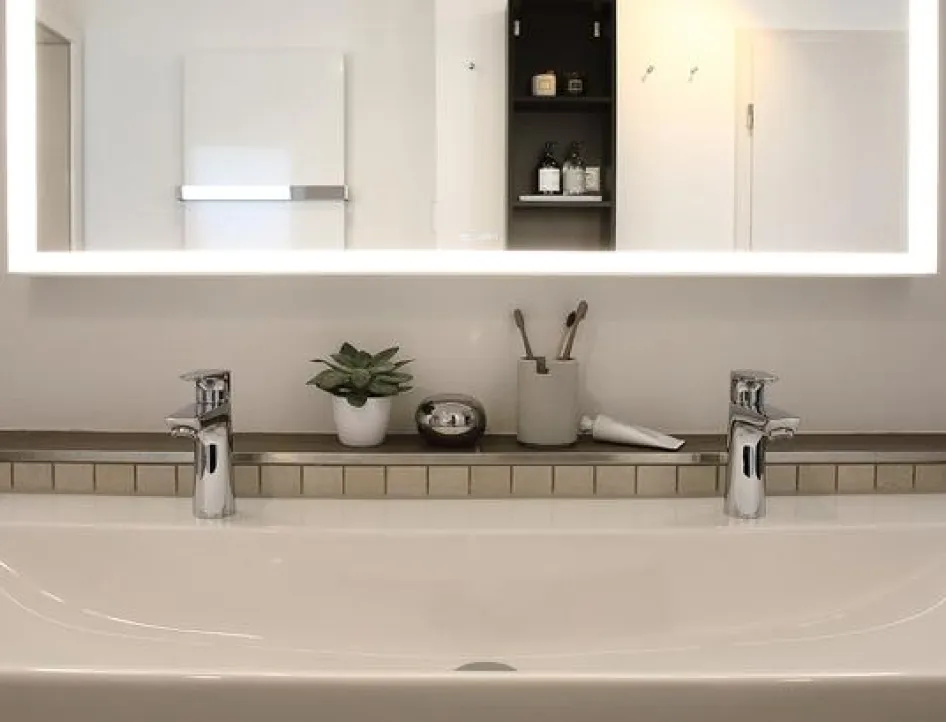 Moderner Doppelwaschtisch mit zwei Armaturen, beleuchtetem Spiegel und stilvoller Ablage im Wellnessbad.