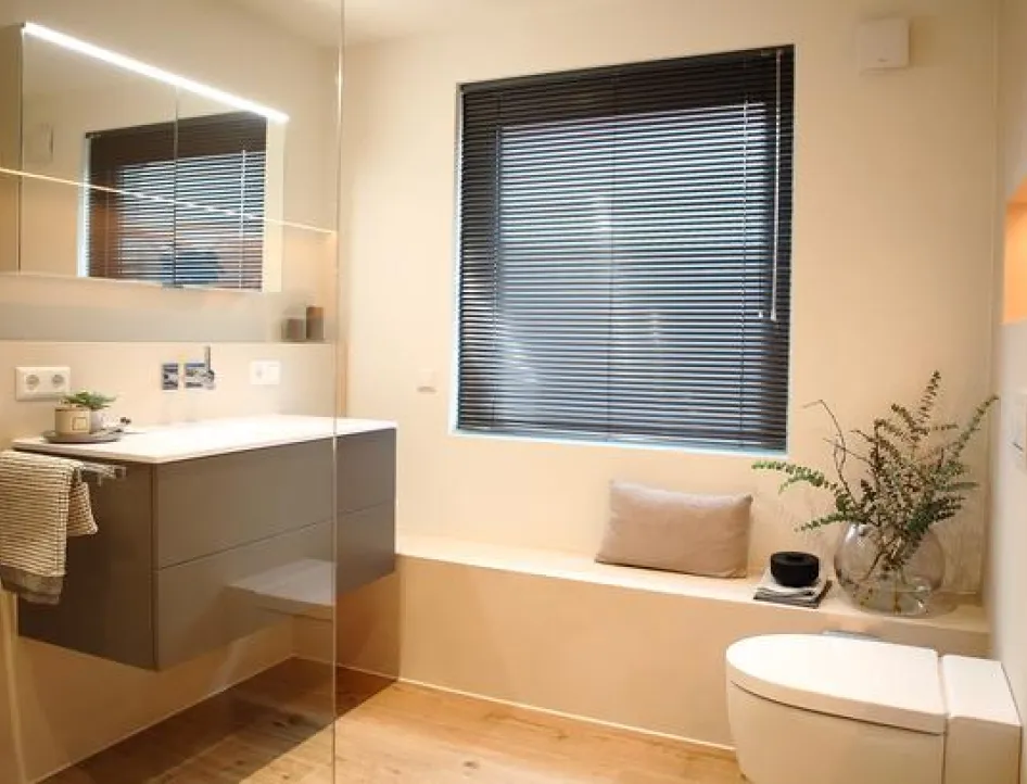 Helles Wohnbad mit schwebendem Waschtisch, großem Spiegel, WC, Fenster mit Jalousie und dekorativer Sitzbank mit Pflanzen.