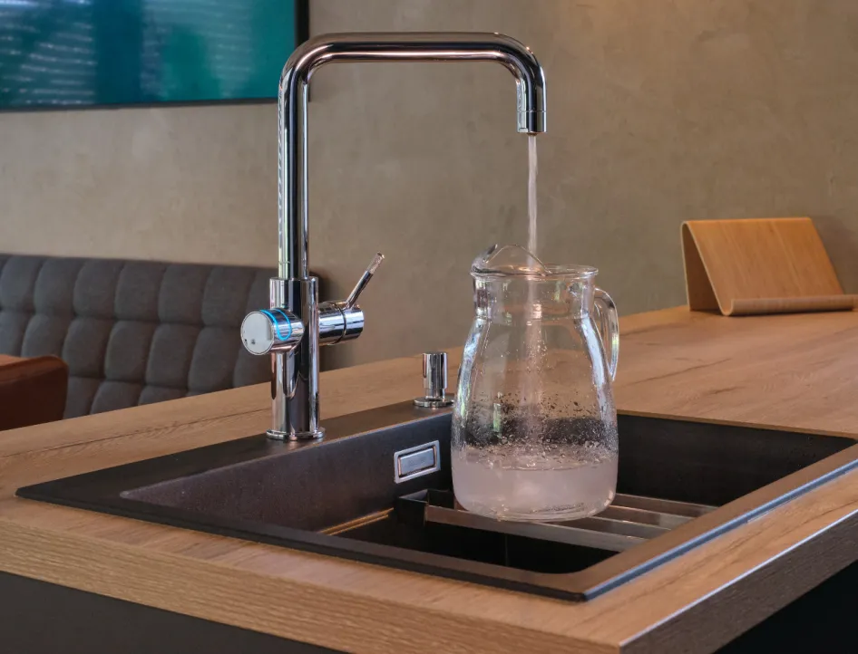 Küchenarmatur auf Kochinsel, die eine Glaskaraffe mit frischem Wasser füllt.