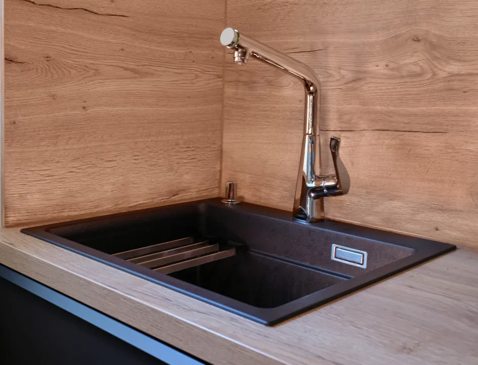 Moderne Küchenspüle mit schwarzer Einbauspüle und verchromter Armatur vor Holzrückwand.